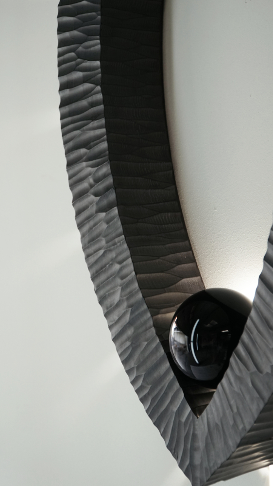 Sculptural wall lamp with an intricate Vesica-inspired geometric design, crafted from wood using fine cabinetmaking techniques. Mounted on a wall, it features a soft, dimmable LED light and a discreet button at the bottom for brightness control.