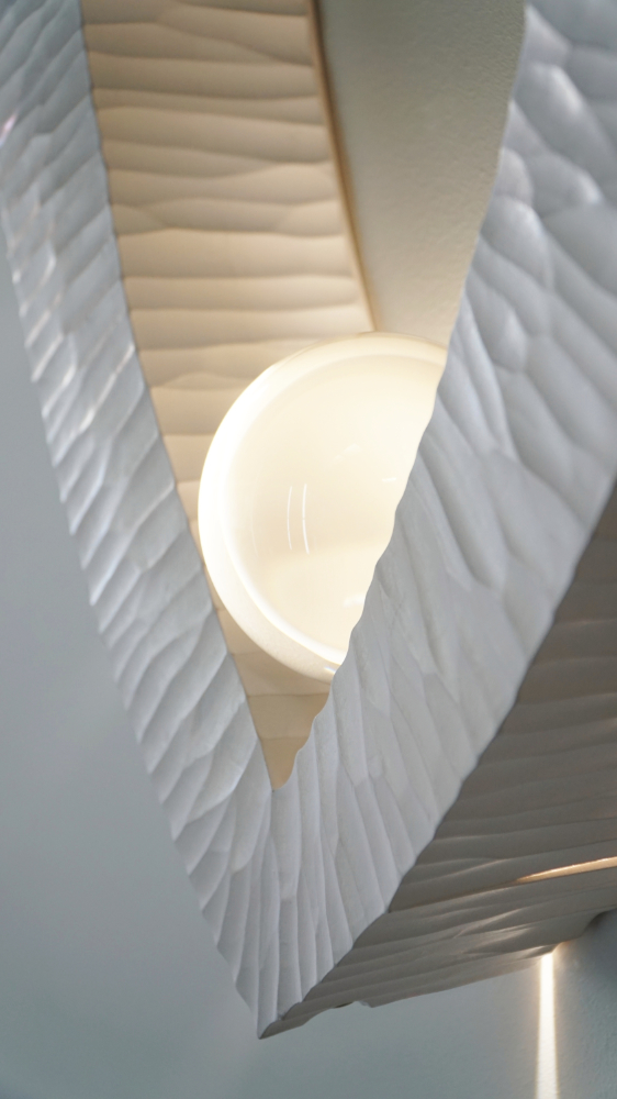 Sculptural wall lamp with an intricate Vesica-inspired geometric design, crafted from wood using fine cabinetmaking techniques. Mounted on a wall, it features a soft, dimmable LED light and a discreet button at the bottom for brightness control.