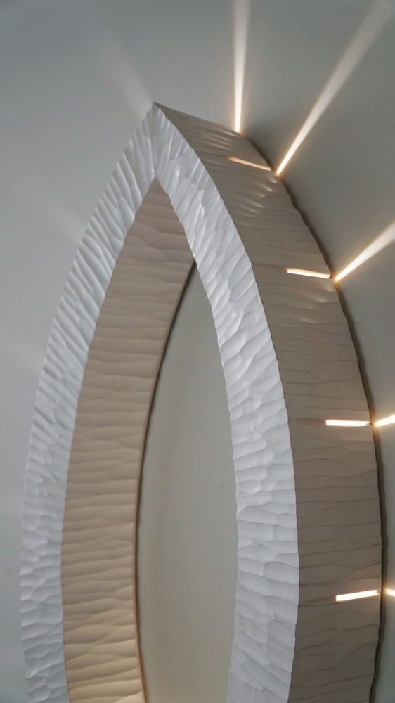 Sculptural wall lamp with an intricate Vesica-inspired geometric design, crafted from wood using fine cabinetmaking techniques. Mounted on a wall, it features a soft, dimmable LED light and a discreet button at the bottom for brightness control.