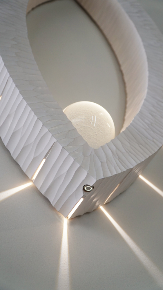 Sculptural wall lamp with an intricate Vesica-inspired geometric design, crafted from wood using fine cabinetmaking techniques. Mounted on a wall, it features a soft, dimmable LED light and a discreet button at the bottom for brightness control.