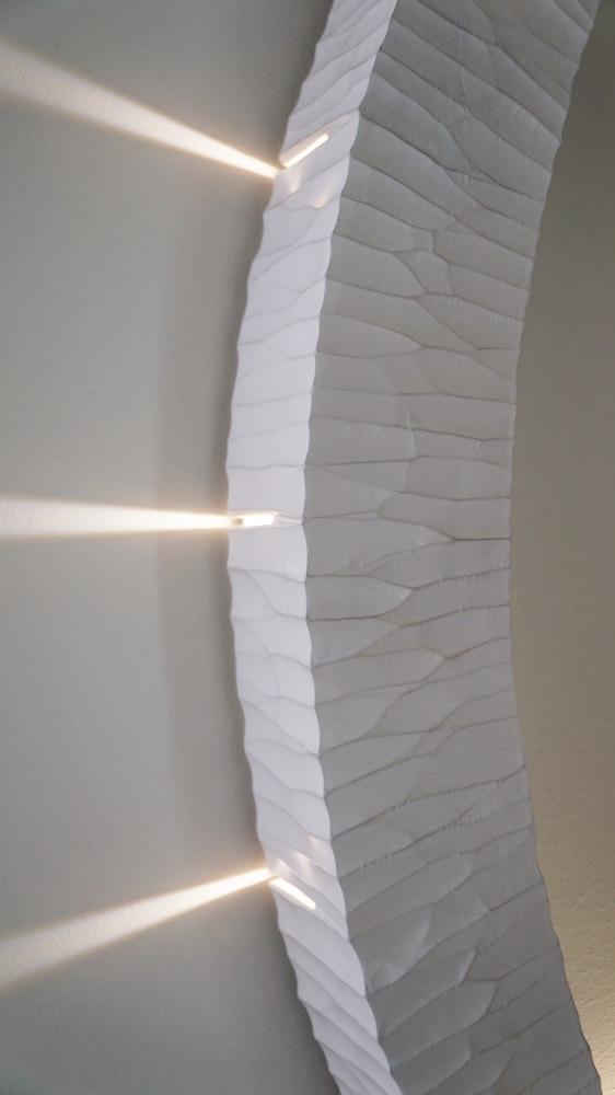 Sculptural wall lamp with an intricate Vesica-inspired geometric design, crafted from wood using fine cabinetmaking techniques. Mounted on a wall, it features a soft, dimmable LED light and a discreet button at the bottom for brightness control.